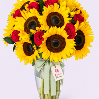Arreglo de rosas rojas y girasoles amarillos en florero de vidrio con moño verde y etiqueta Flores Bellas.